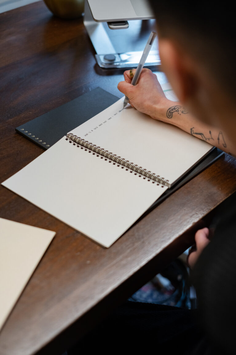 A non-binary person writing in a notebook