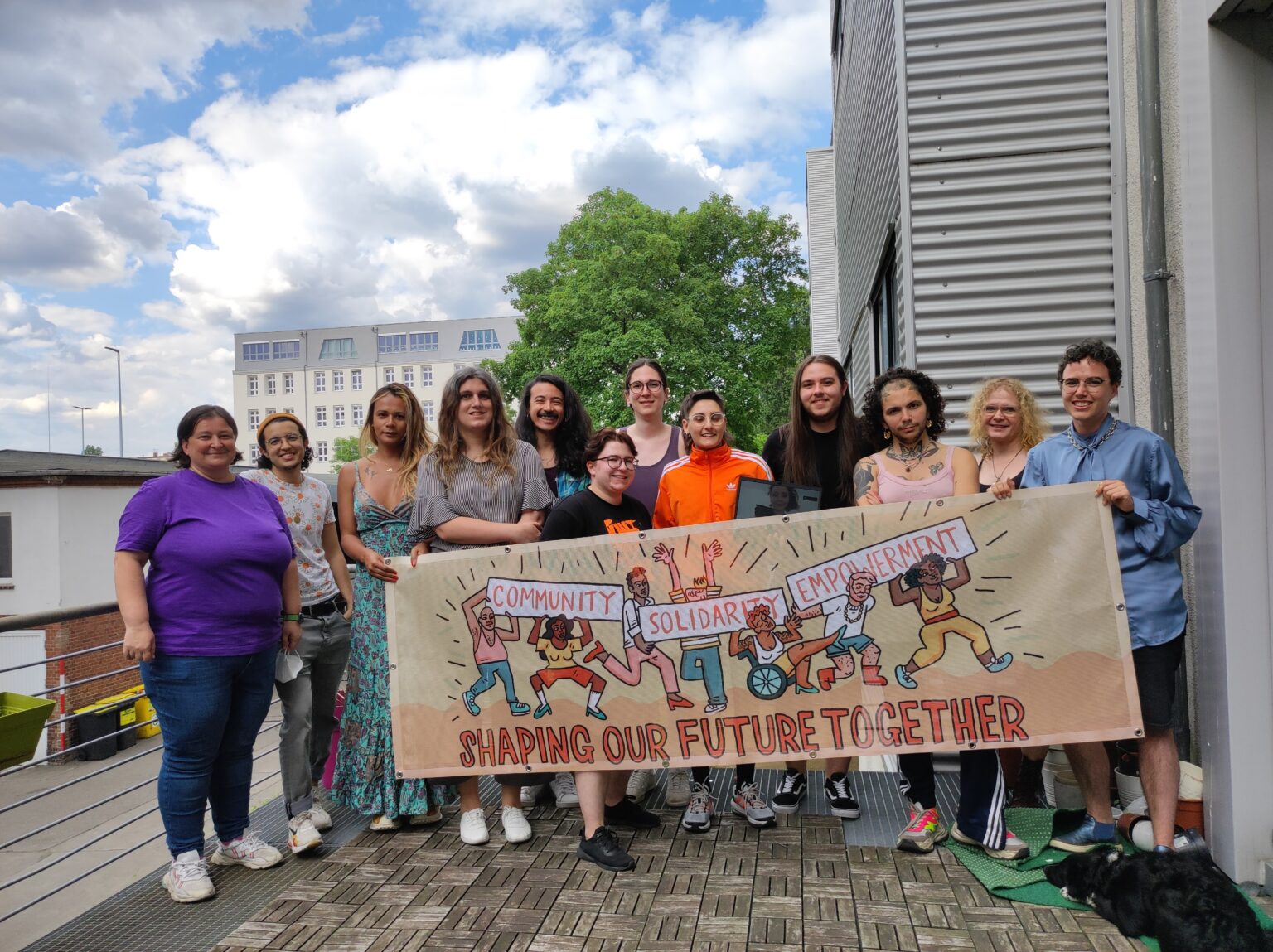 A group of trans people outside TGEU holding a banner saying: Community Solidarity Empowerment -- Shaping our future together.