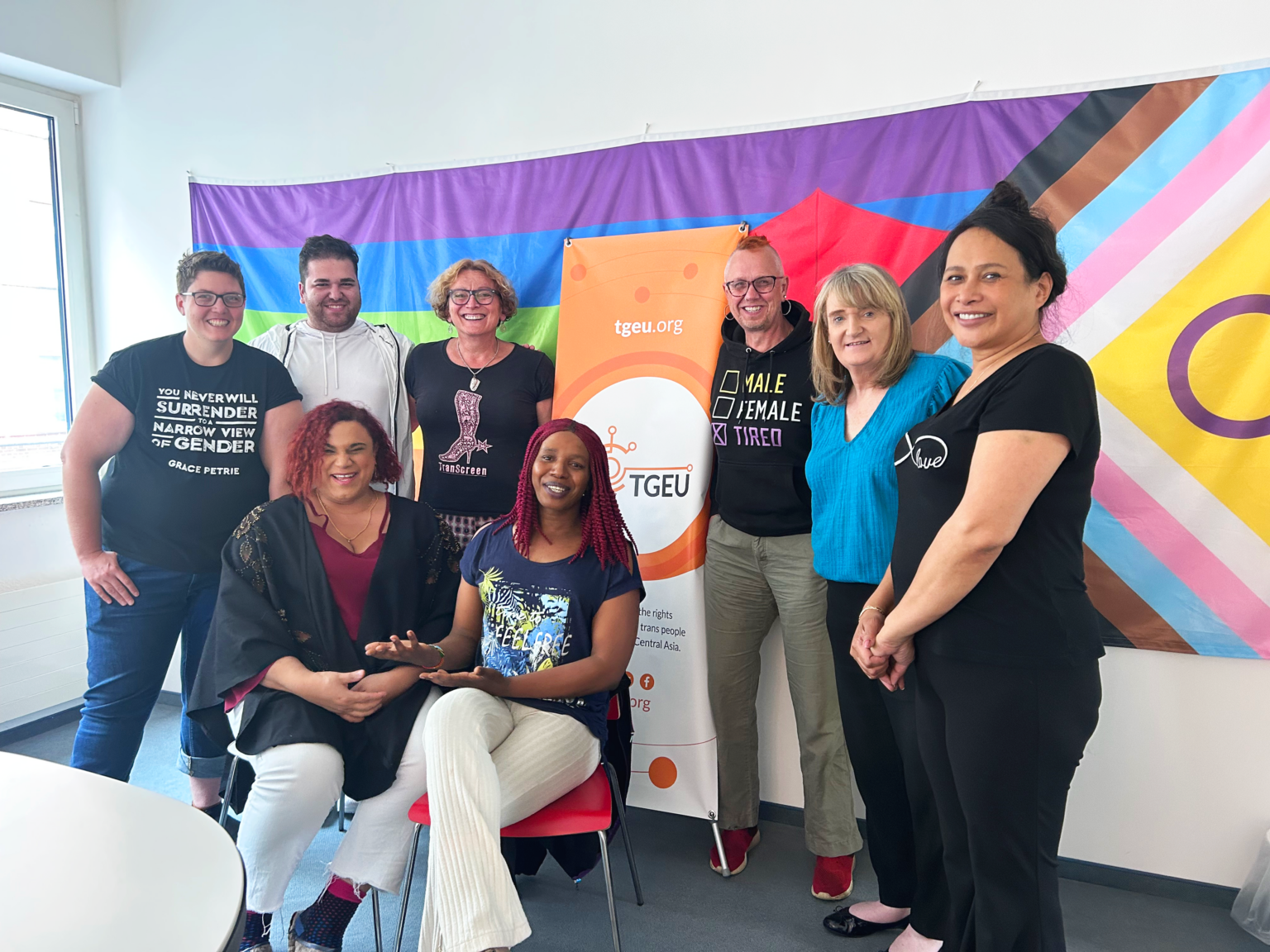 TGEU's two co-chairs and six board members in front of the inclusive pride flag in 2023.
