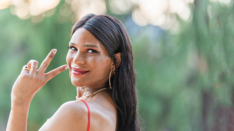 A trans woman smiles over her shoulder holding up the peace sign.