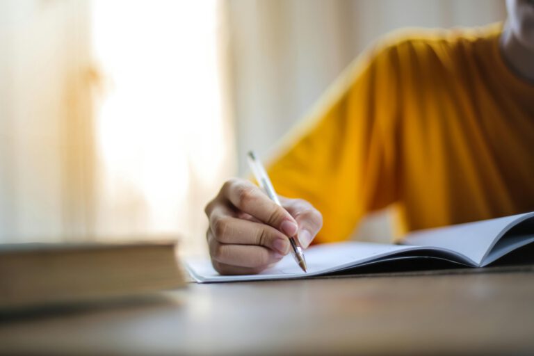 Person wearing a yellow top, writing by hand at a desk