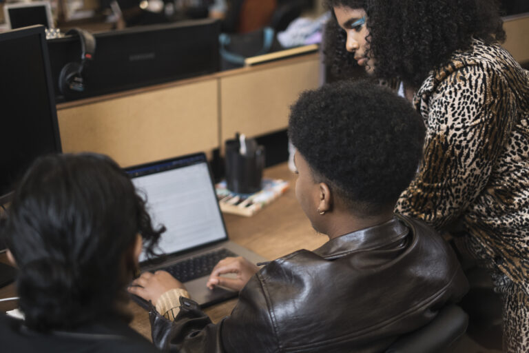 A group of people of varying genders working on a laptop.
